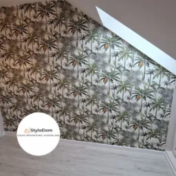 Pokój na poddaszu z tapetą w tropikalne palmy, widoczne białe drzwi z przeszkleniami, szara roleta okienna i lampa z motywem sów.