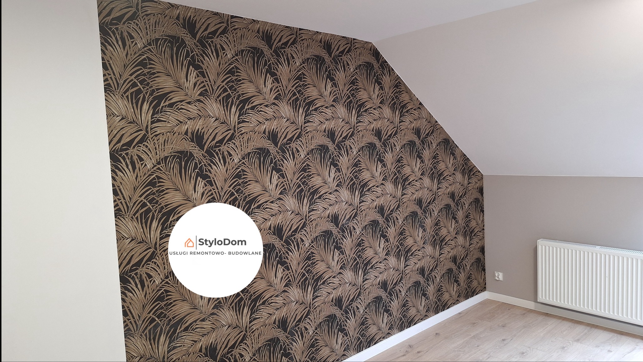 Ściana w pokoju na poddaszu wykończona tapetą w złote liście na czarnym tle, kontrastująca z białą, skośną ścianą i jasną podłogą, widoczny grzejnik.