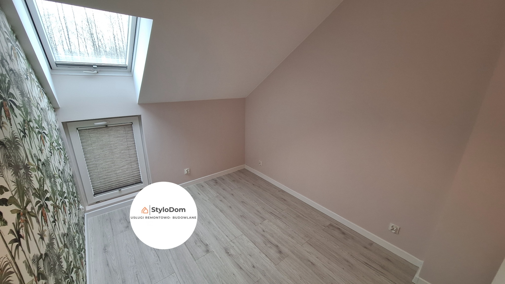Poddasze po remoncie: ściana w kolorze pudrowego różu, jasne panele podłogowe imitujące drewno, okno dachowe z widokiem na drzewa i okno pionowe z żaluzjami, ściana z tapetą w motywy roślinne.