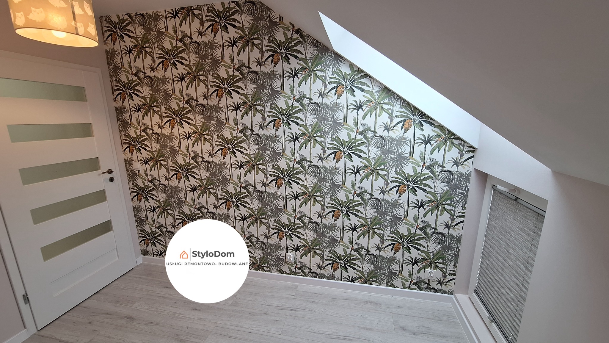 Pokój na poddaszu z tapetą w tropikalne palmy, widoczne białe drzwi z przeszkleniami, szara roleta okienna i lampa z motywem sów.