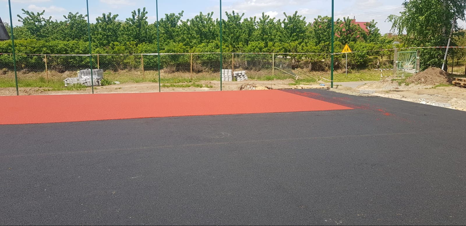 Nawierzchnia sportowa z czerwonym i czarnym poliuretanem, widoczne przygotowane obrzeża i materiały budowlane w tle.