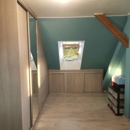 MARCIN KOŁODZIEJCZAK - Adaptacja poddasza ze skośnym oknem dachowym i zabudową szaf z przesuwnymi drzwiami w jasnym odcieniu drewna.