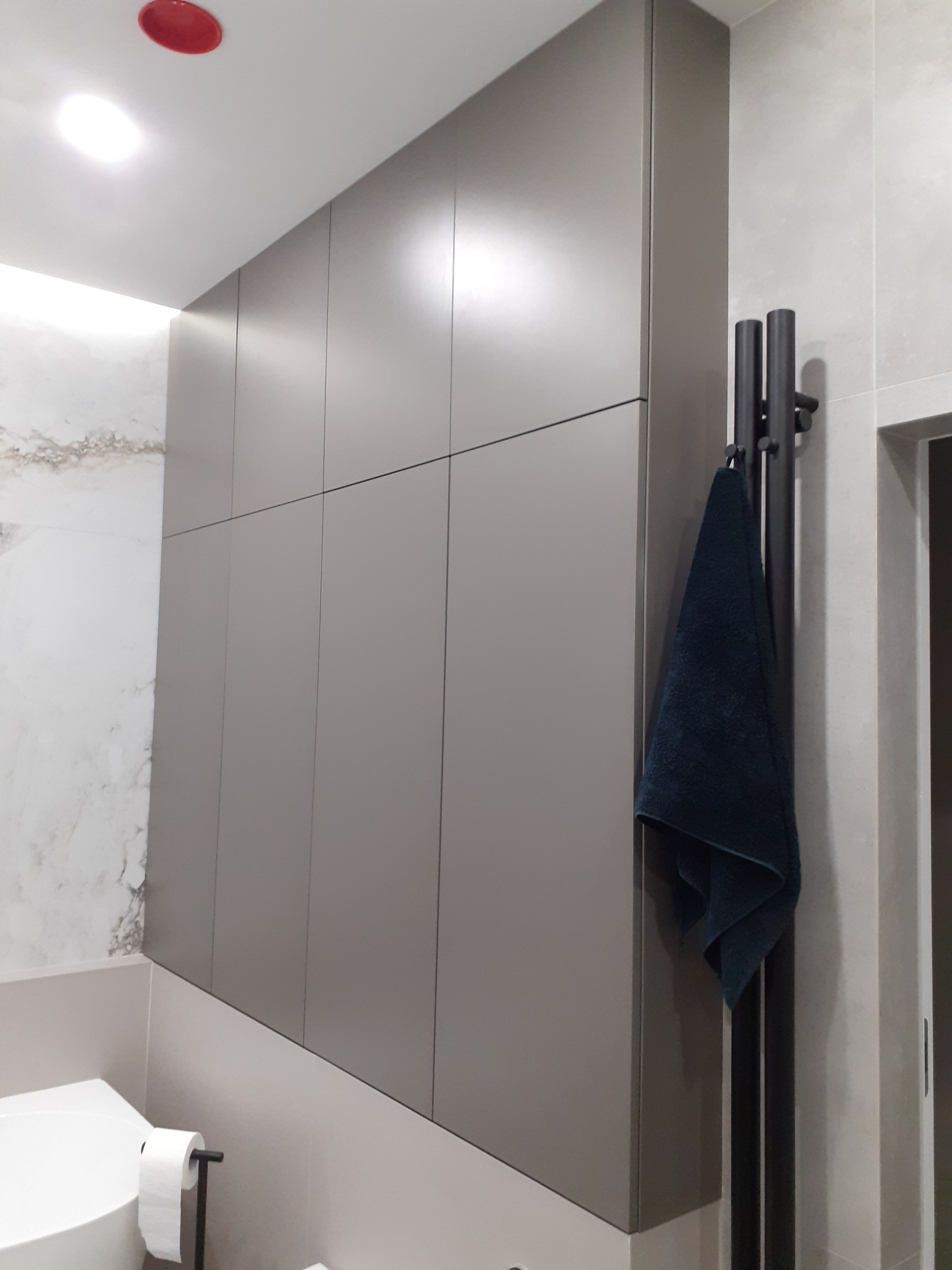 Szara szafa na wymiar w łazience w Miejskie Górce, z ciemnym ręcznikiem na czarnym wieszaku, widok z boku na tle marmurowych płytek.