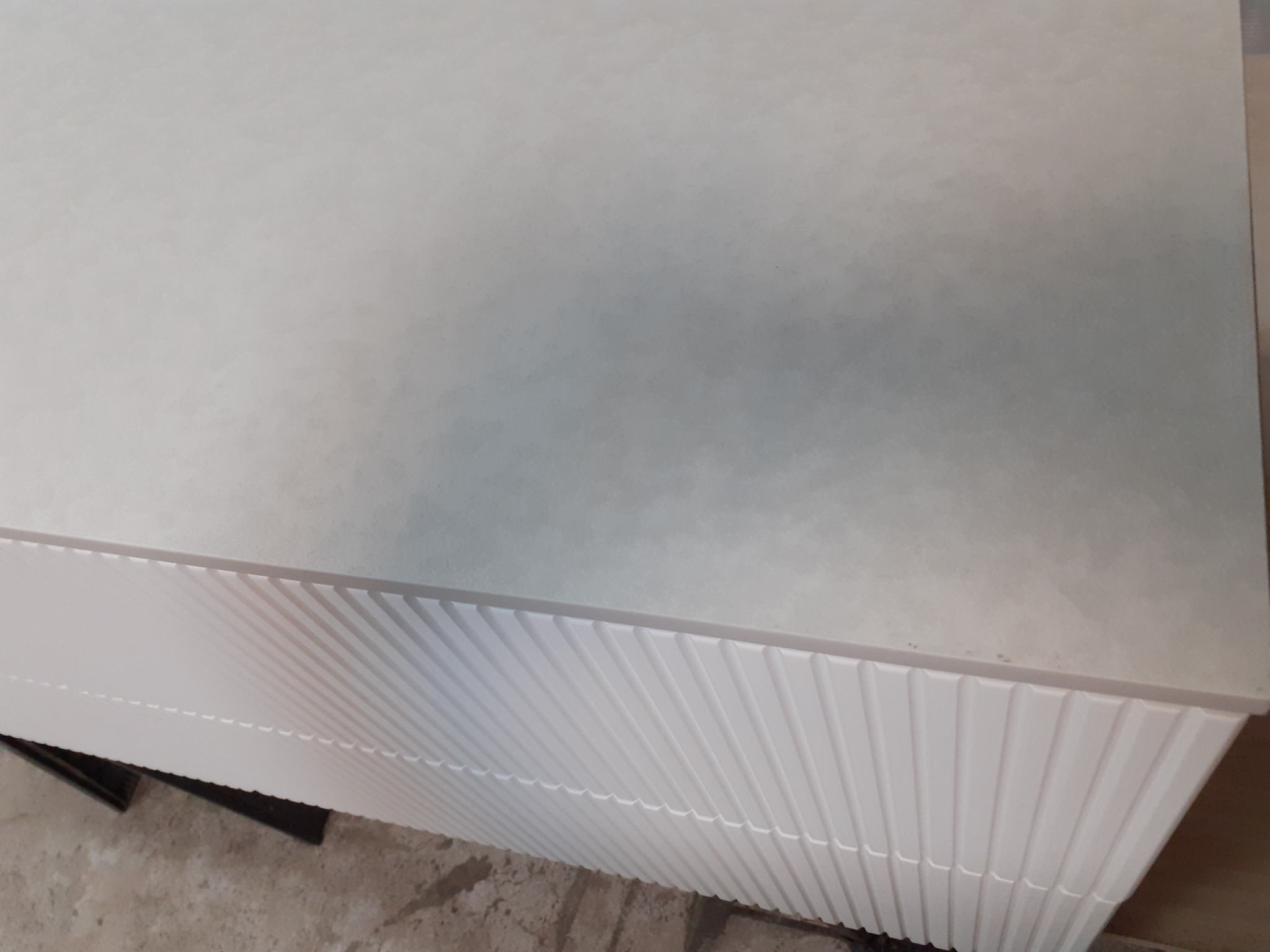 Fragment szafki z białymi, żłobionymi frontami i szarym blatem, widziana z góry pod kątem.