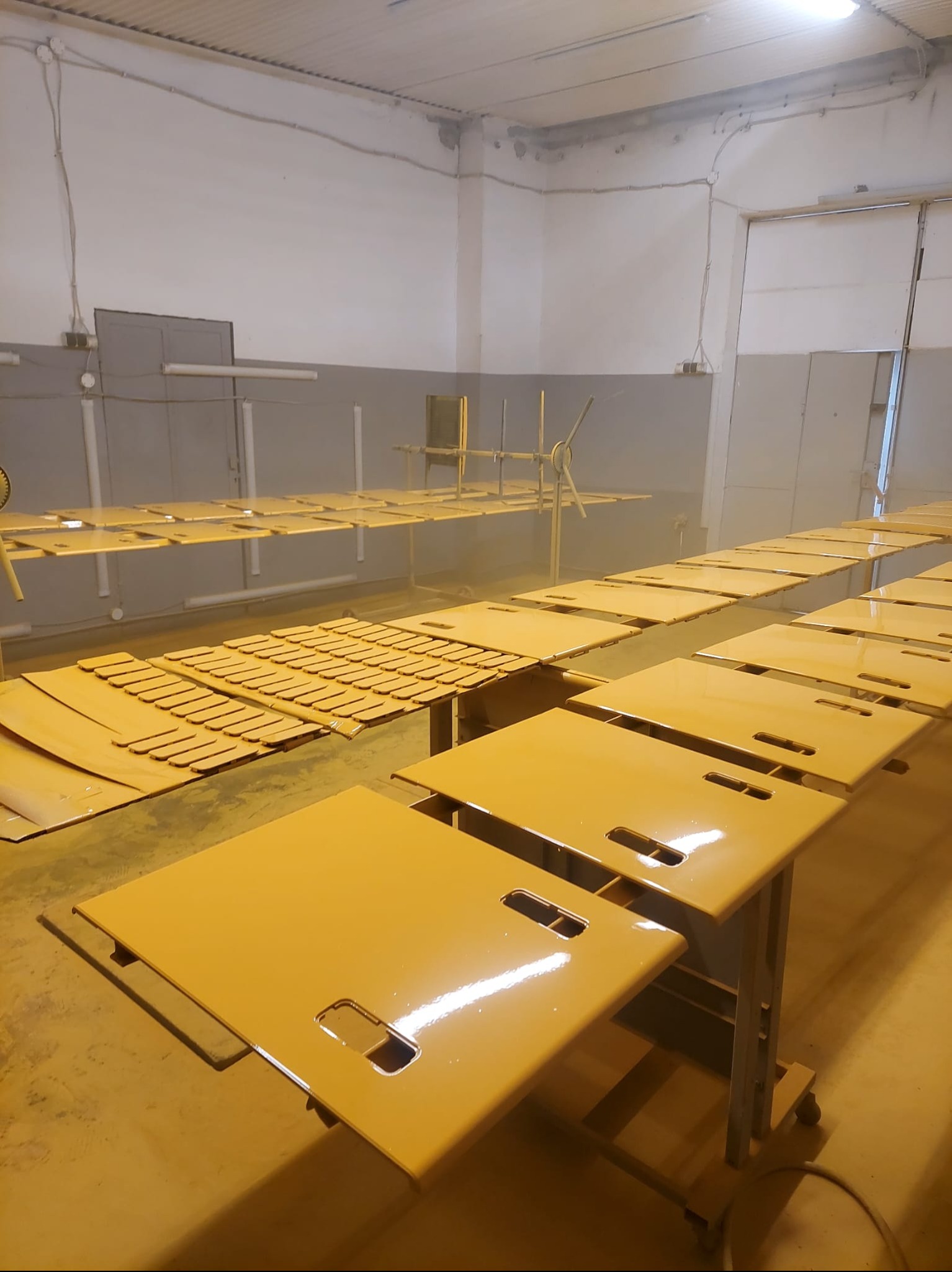 Elementy metalowe po lakierowaniu na żółto w hali we Wrocławiu. Widoczne detale z otworami, równomiernie pokryte farbą, ustawione na stołach w przestrzeni warsztatowej.