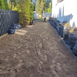 Pan Ogrodnik - Przygotowany teren pod ogród po użyciu glebogryzarki, z workami z resztkami roślinnymi ustawionymi wzdłuż ogrodzenia i ściany budynku.