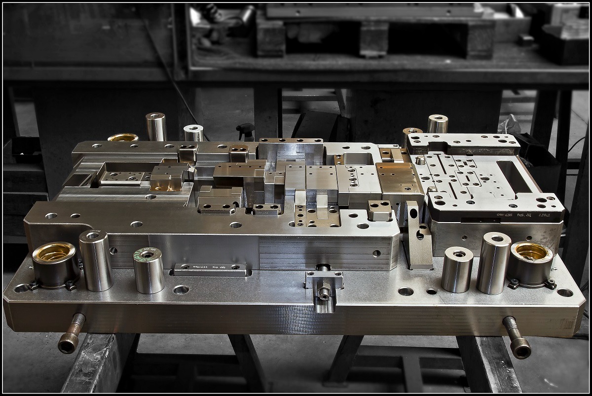 Precyzyjna forma wtryskowa z metalu, widoczne elementy składowe, cylindryczne prowadnice i mocowania, ustawiona na metalowym stole w warsztacie.