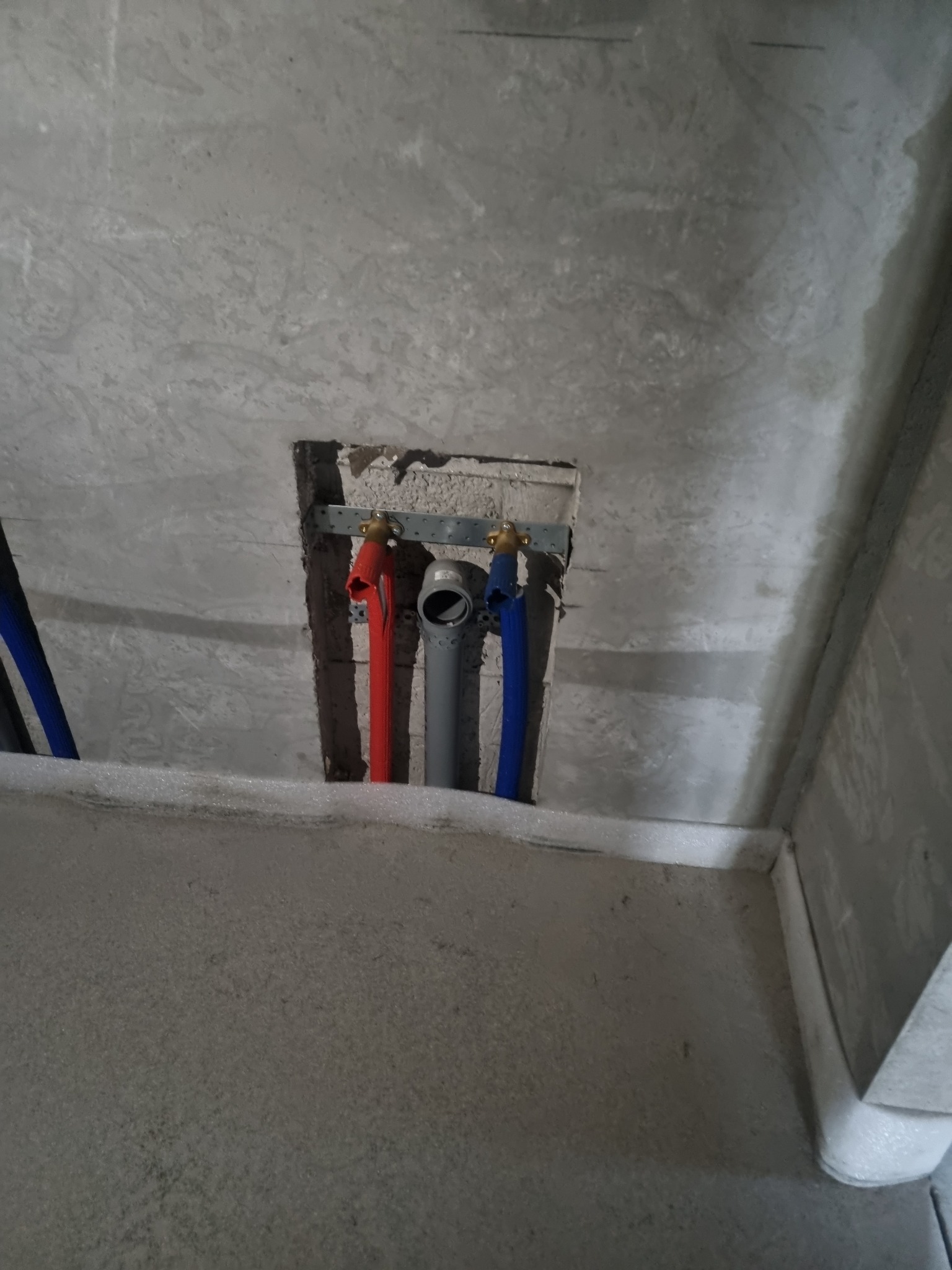 Fragment sufitu z otworem, w którym widoczne są rury instalacyjne: czerwona, szara i niebieska, zamocowane na metalowej listwie.