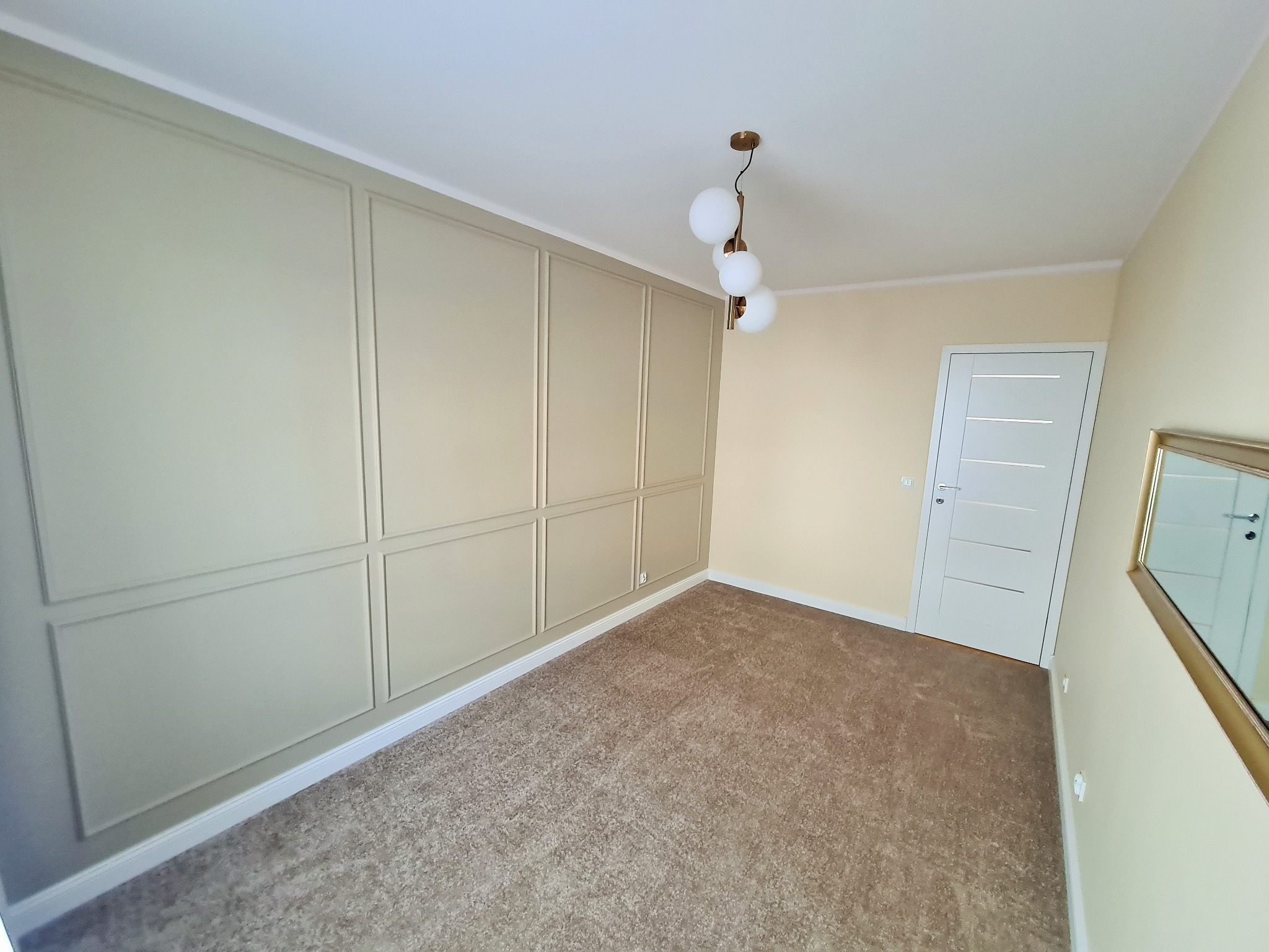 Pomalowane wnętrze pokoju z beżowymi ścianami, sztukaterią w kolorze khaki, brązowym dywanem i nowoczesną lampą wiszącą z trzema kulami.