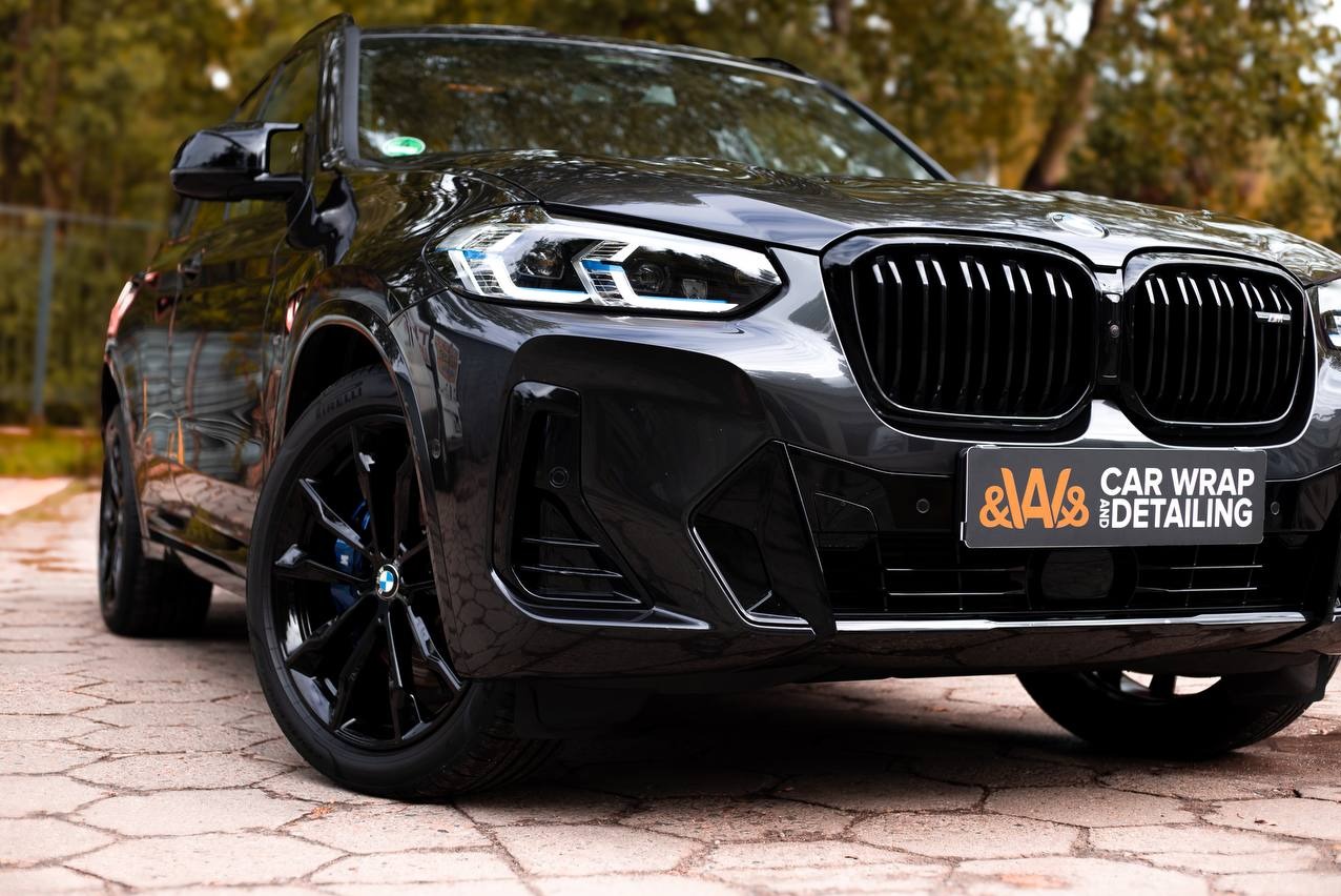 Czarny samochód BMW X3 po zabiegu detailingu, z widocznym logo firmy detailingowej na przednim zderzaku.