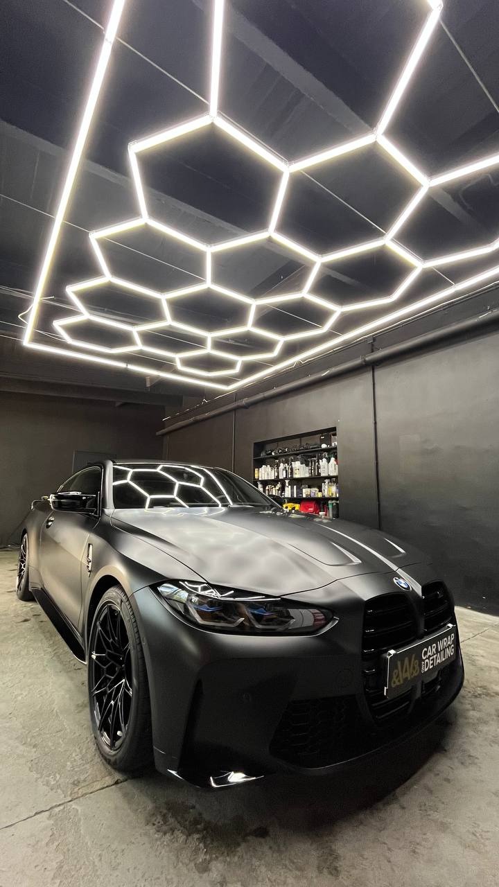 Matowy, czarny samochód BMW M4 po zabiegu detailingu, oświetlony heksagonalnymi lampami LED w profesjonalnym studiu.
