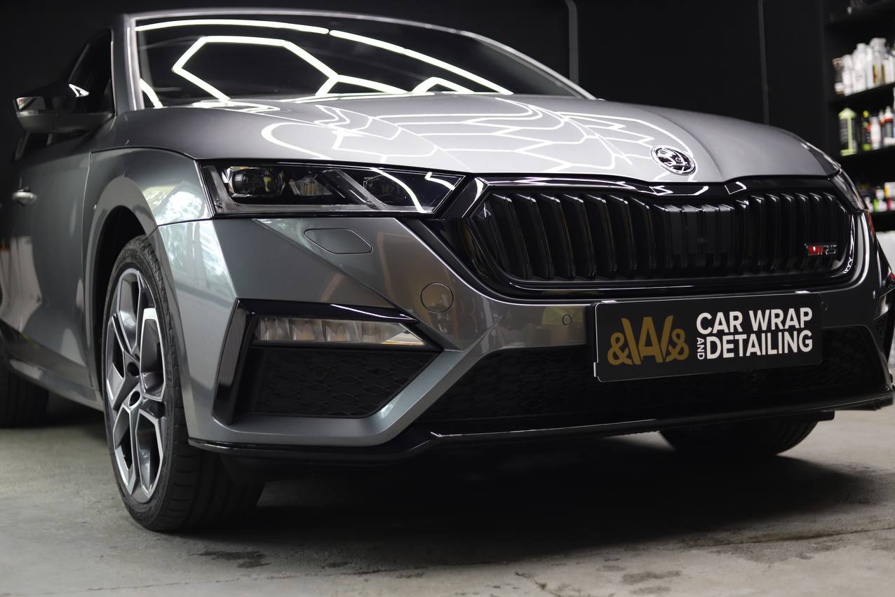 Szary samochód Skoda Octavia RS po oklejeniu folią, z widocznym logo firmy detailingowej na tablicy rejestracyjnej.