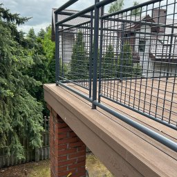Andrzej Szymański - Nowoczesny taras kompozytowy z szarą metalową balustradą, wsparty na ceglanym filarze. Widok na dom i zieleń. Ujęcie z góry, podkreślające detale wykończenia.