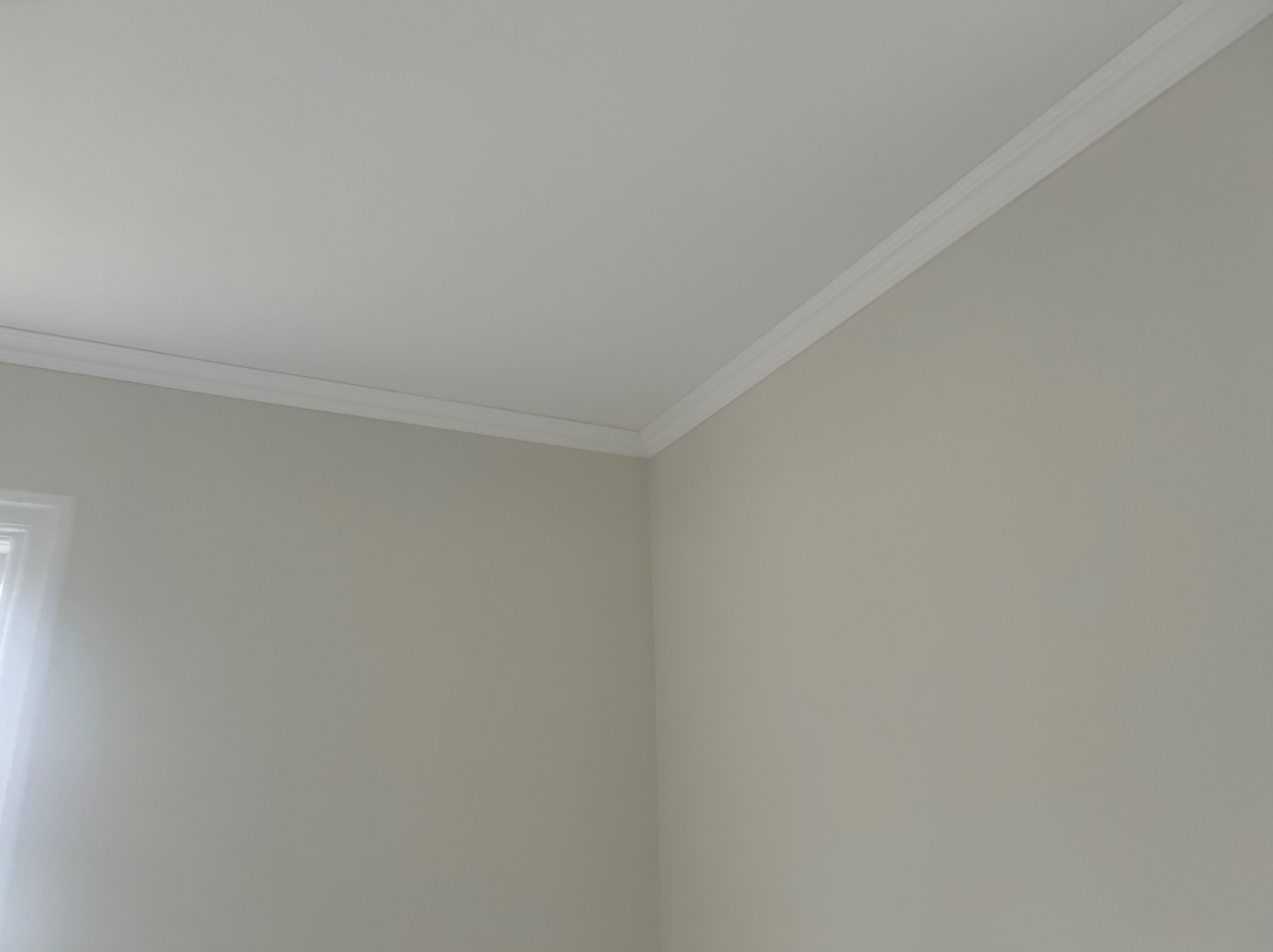 Jasne, świeżo pomalowane wnętrze z dekoracyjną listwą przysufitową. Minimalistyczny design, neutralna kolorystyka ścian i subtelne światło wpadające przez okno.