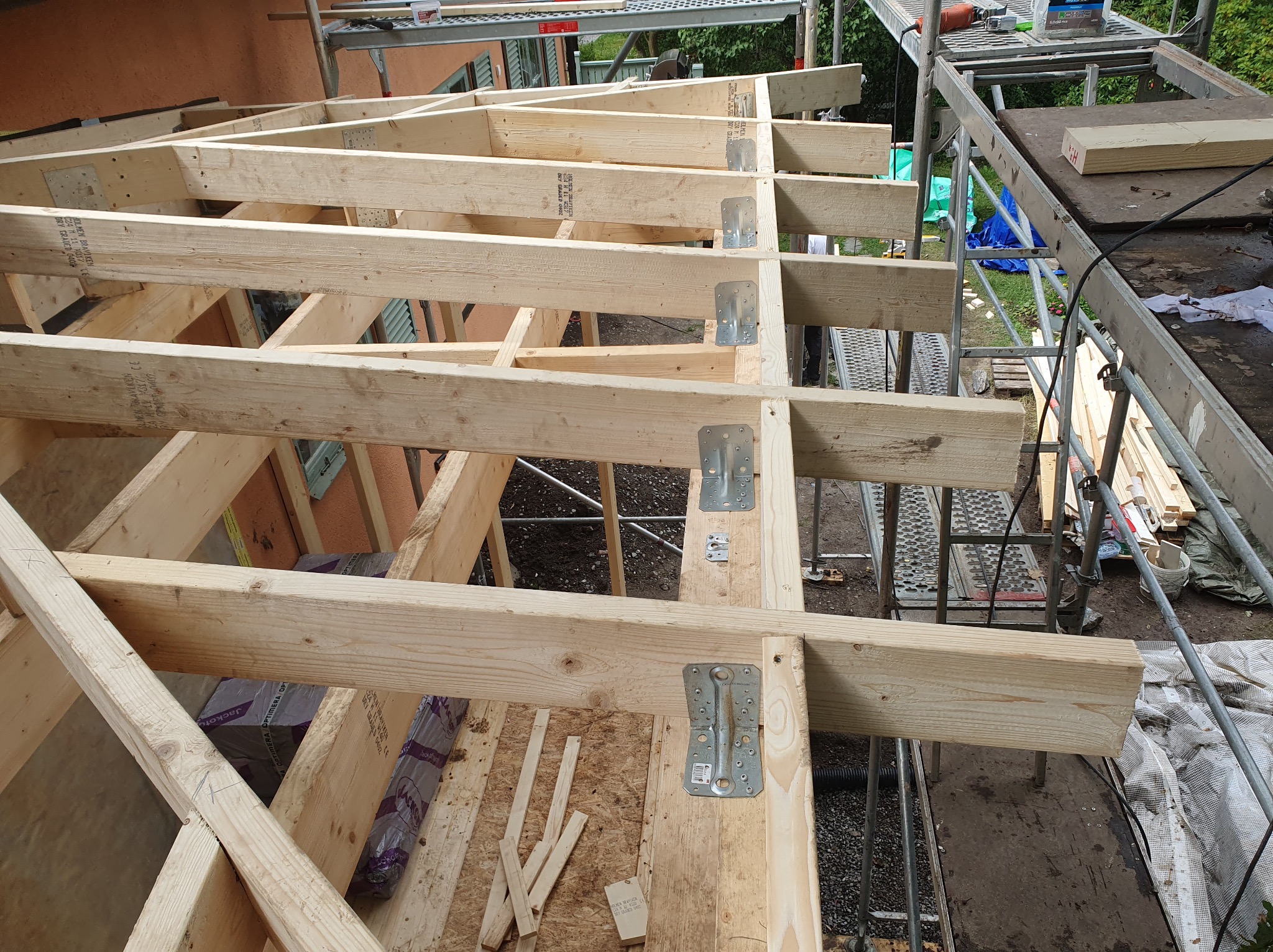 Konstrukcja drewniana dachu z widocznymi metalowymi łącznikami, rusztowania w tle. Realizacja w Kaliszu.