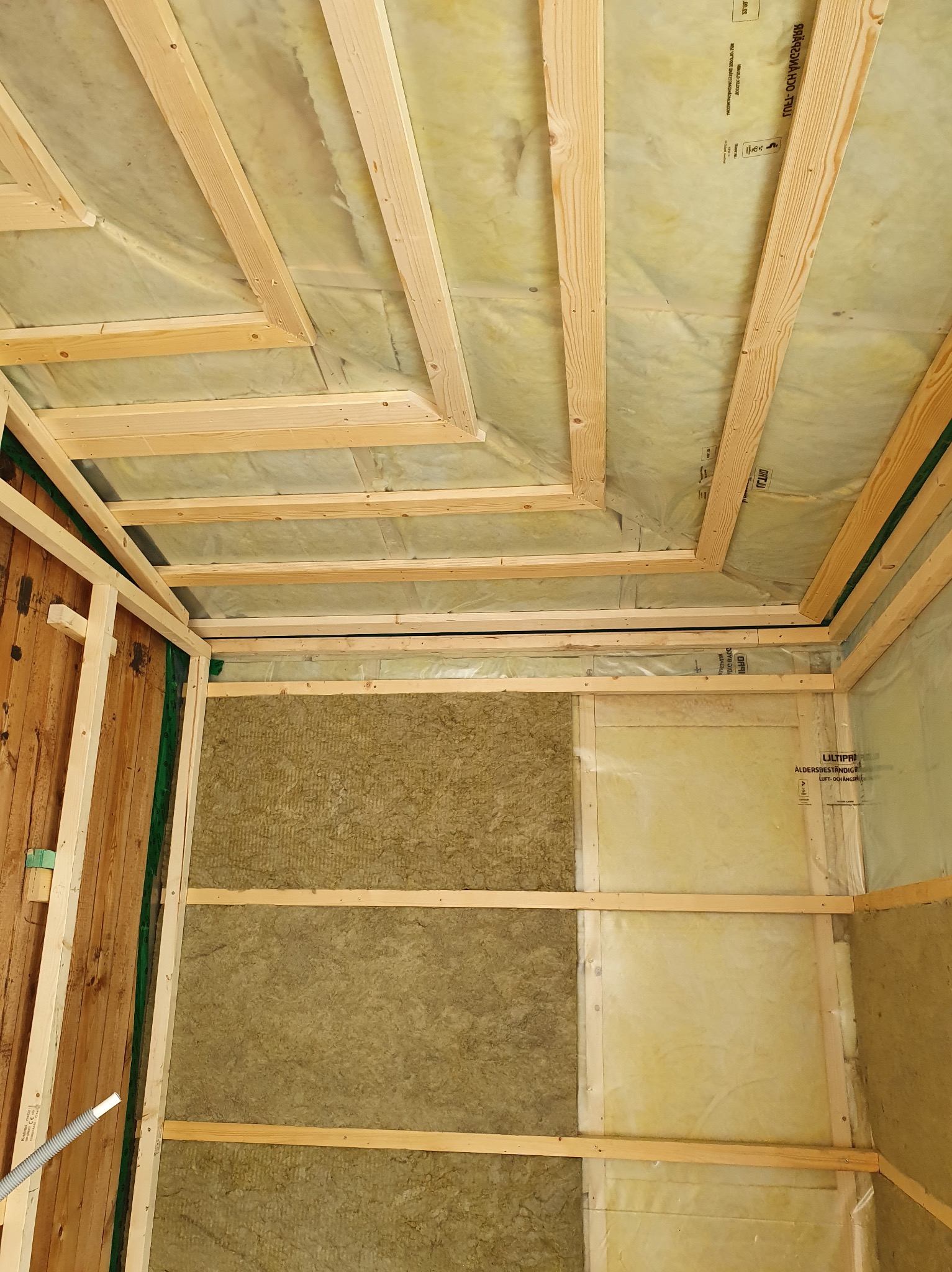 Wnętrze w trakcie izolacji: drewniana konstrukcja szkieletowa, wełna mineralna i folia paroizolacyjna. Widoczne fragmenty starej drewnianej ściany.