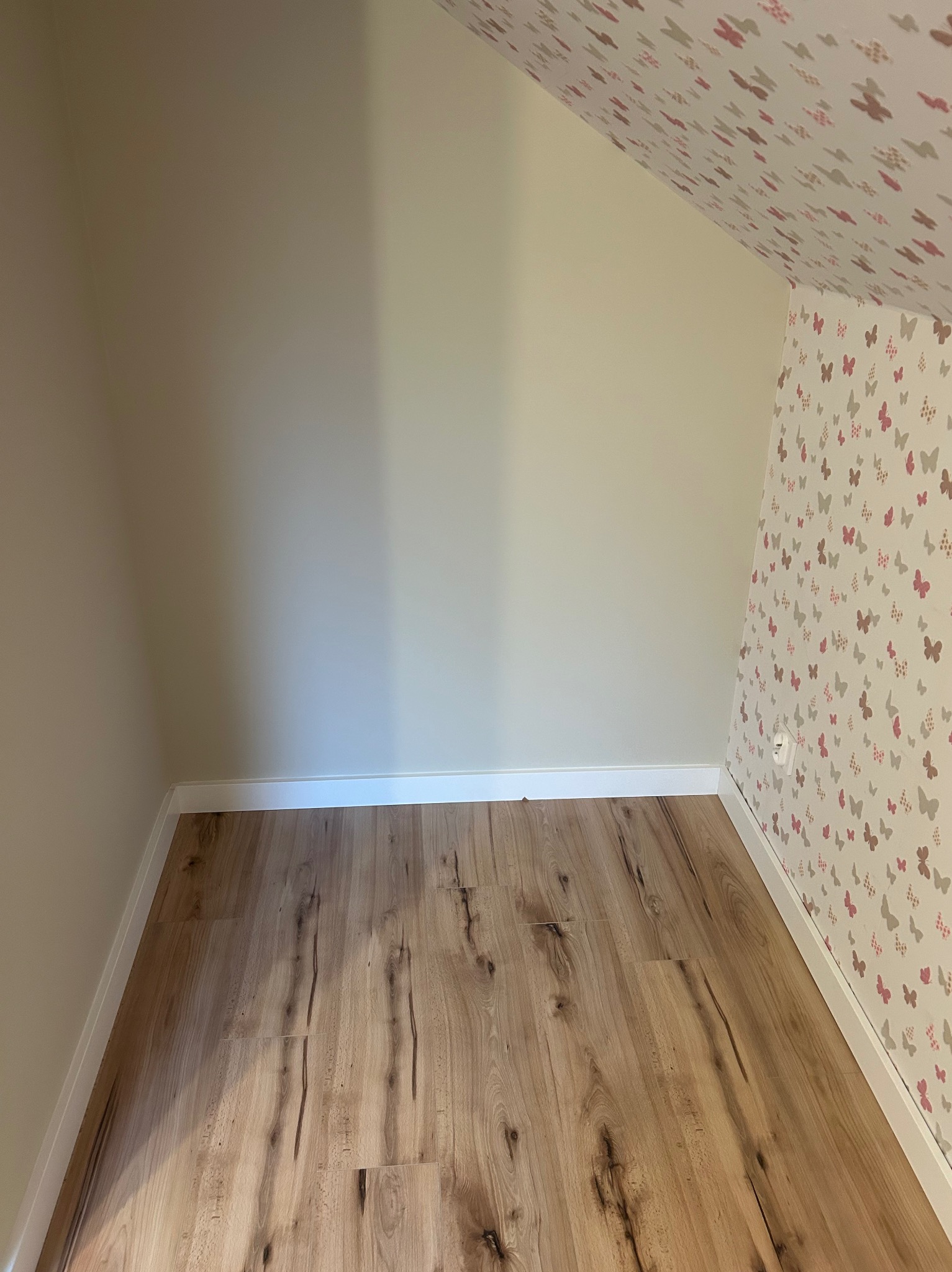 Pokój na poddaszu po remoncie: panele podłogowe, ściana pomalowana na beżowo, ściana i sufit w motyle. Widoczne listwy przypodłogowe.