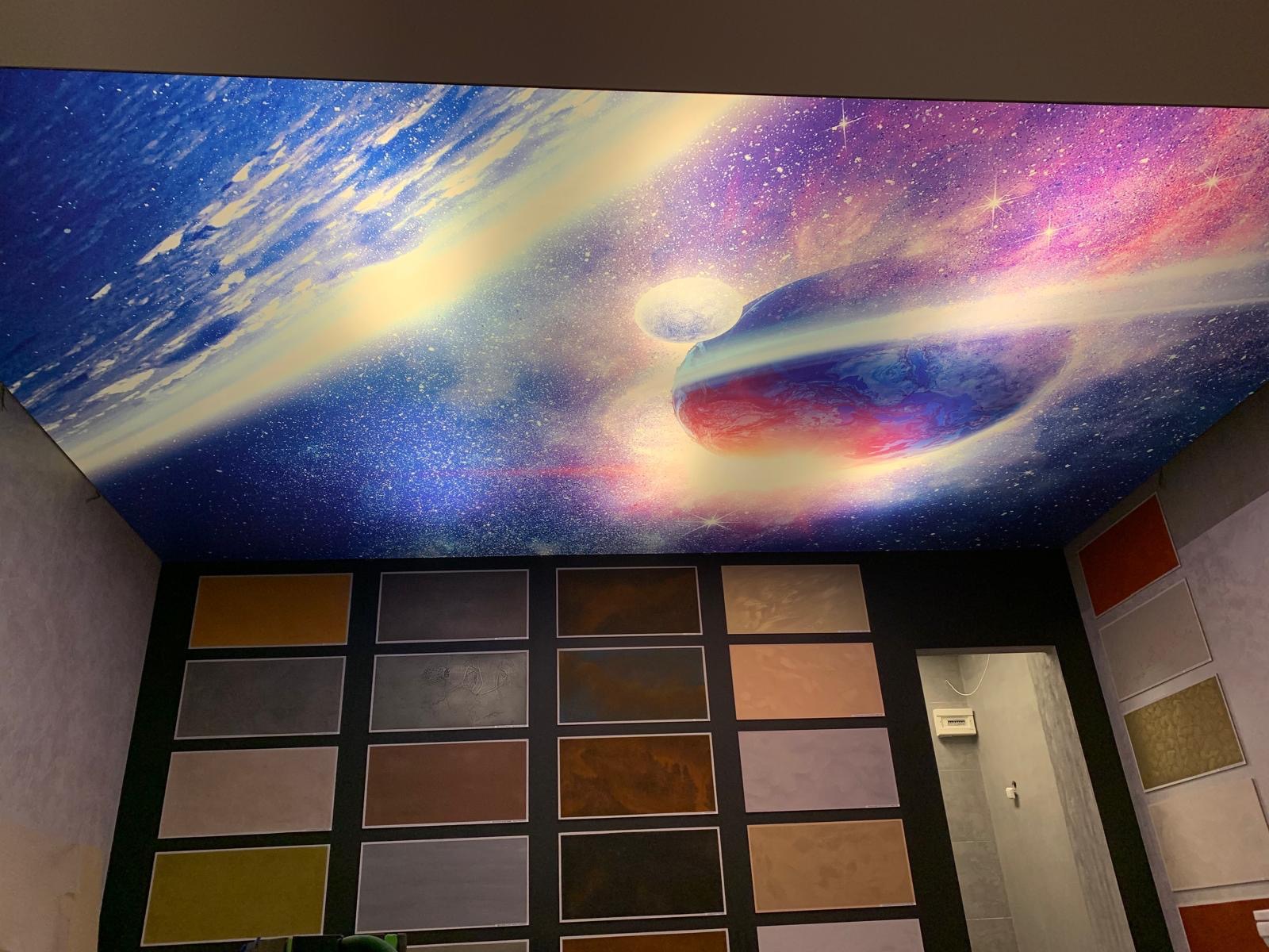 Sufit napinany z motywem kosmosu, z widoczną planetą i gwiazdami, w pomieszczeniu z ekspozycją próbek różnych kolorów i faktur na ścianie.