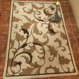 Beżowy dywan z brązowym, roślinnym wzorem czyszczony odkurzaczem piorącym na brązowej, kwadratowej podłodze z płytek.