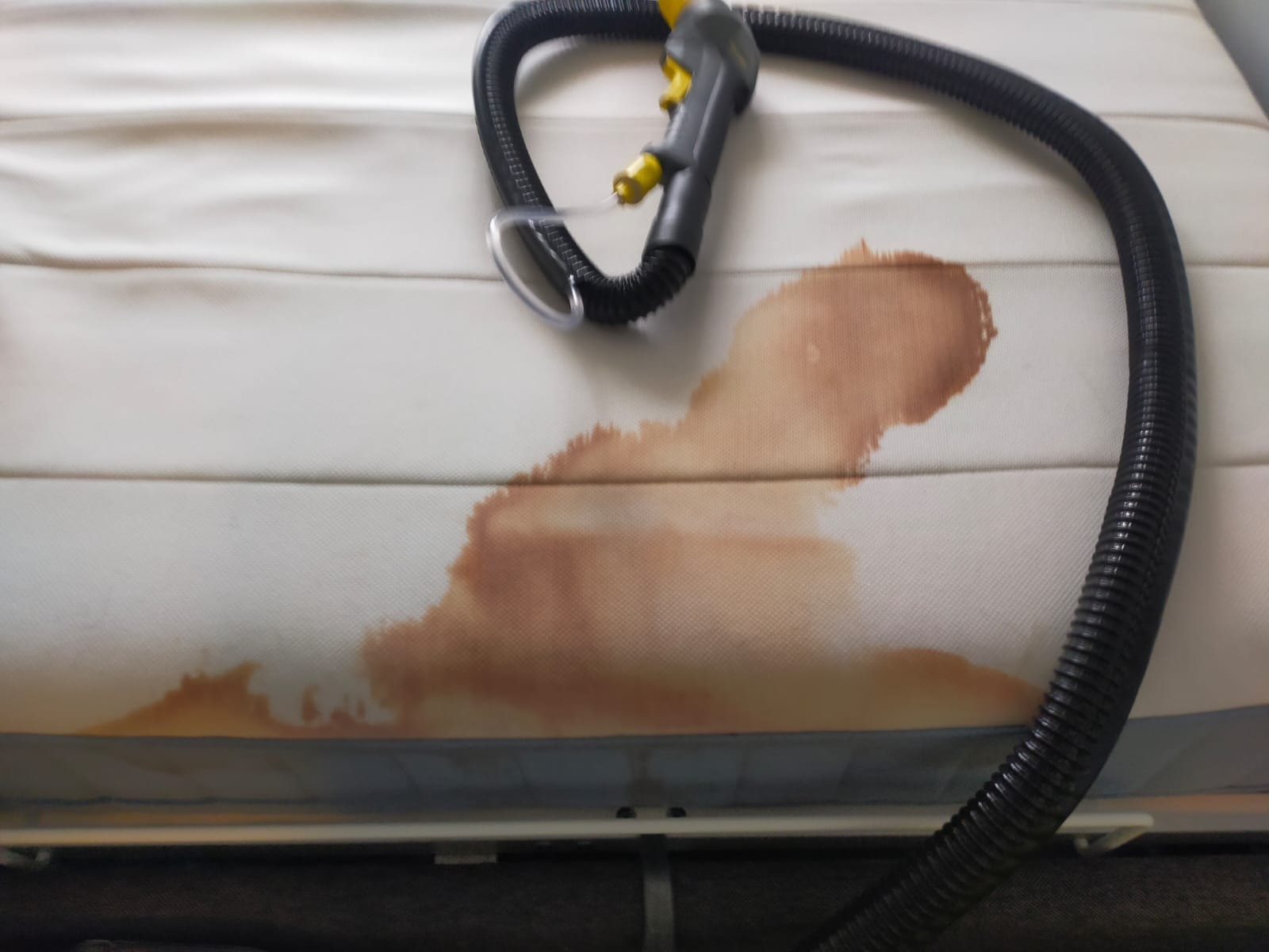 Czyszczenie materaca z widocznym, brązowym zabrudzeniem i dyszą odkurzacza piorącego, ukazującą etap usuwania plamy.