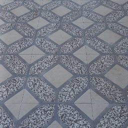 SOFIIA VIKHARIEVA - Wzór podłogi z płytek ceramicznych w odcieniach szarości i beżu, z motywem łączących się rombów i wypełnieniem z drobnych kamyczków, oraz gumka recepturka leżąca na płytkach w dolnej części kadru.