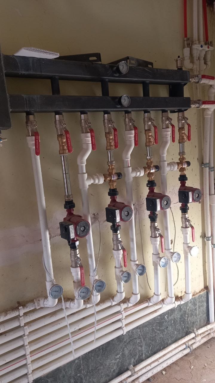 Rozdzielacz centralnego ogrzewania z pompami obiegowymi i zaworami, zamontowany na ścianie w kotłowni.