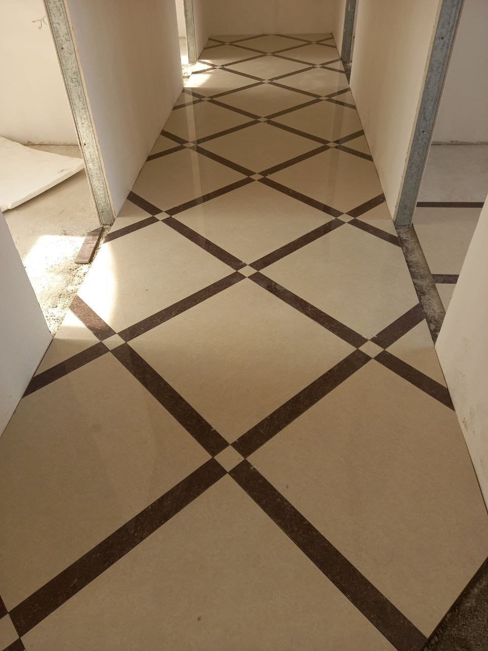 Nowo położona, beżowa podłoga z ciemnobrązowym wzorem w romby, widoczna w korytarzu w trakcie remontu, z surowymi ścianami i metalowymi profilami.
