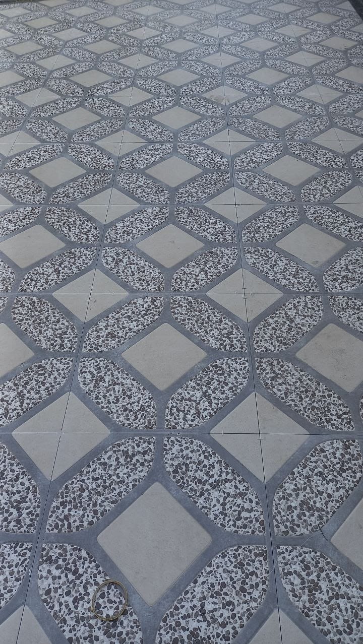 Wzór podłogi z płytek ceramicznych w odcieniach szarości i beżu, z motywem łączących się rombów i wypełnieniem z drobnych kamyczków, oraz gumka recepturka leżąca na płytkach w dolnej części kadru.