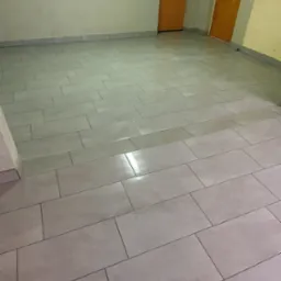 Ułożone, prostokątne, szare płytki podłogowe w pomieszczeniu z dwoma drewnianymi drzwiami i aluminiową drabiną wiszącą na ścianie.