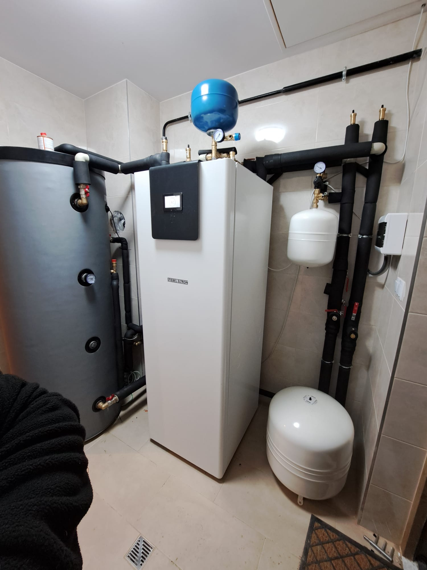 Zainstalowana gruntowa pompa ciepła Stiebel Eltron o mocy 7,35 kW w kotłowni, z widocznym buforem CO o pojemności 500 litrów, czarnymi rurami izolowanymi termicznie i manometrami.