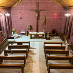 Wnętrze kaplicy w Łące: widok z góry na drewniane ławki, marmurową posadzkę i ceglane ściany z krucyfiksem.