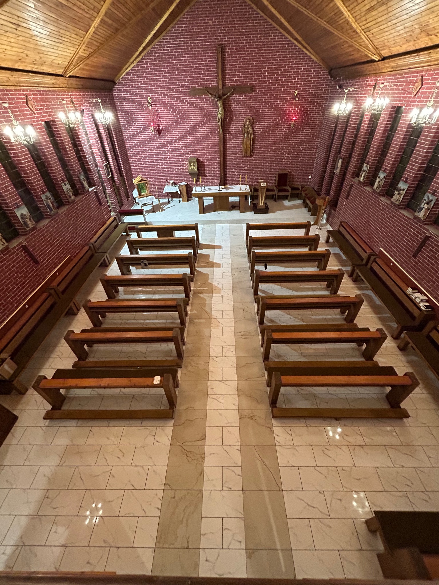 Wnętrze kościoła z drewnianym stropem i ceglanymi ścianami, z rzędami drewnianych ławek na marmurowej posadzce.