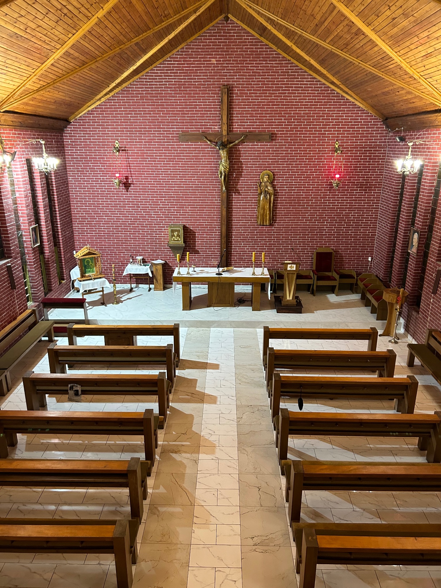 Wnętrze kaplicy w Łące: widok z góry na drewniane ławki, marmurową posadzkę i ceglane ściany z krucyfiksem.