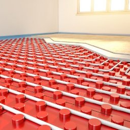 Raccoon services - Instalacja ogrzewania podłogowego z czerwonymi mocowaniami i białymi rurkami w trakcie montażu, widoczny fragment wylewki i okno w tle.