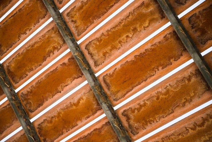 Fragment instalacji z panelami w kolorze bursztynowym, oddzielonymi białymi liniami i metalowymi wspornikami, widok z dołu pod kątem.