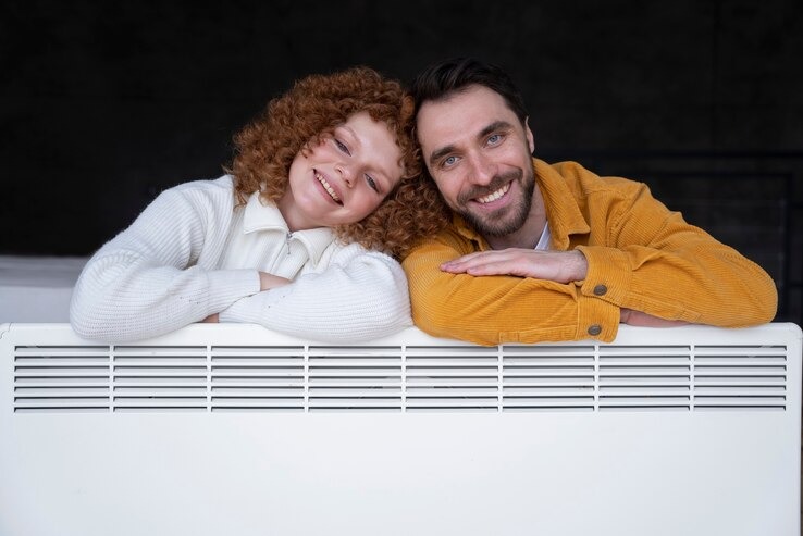 Uśmiechnięta para opiera się o biały, nowoczesny grzejnik panelowy w mieszkaniu.