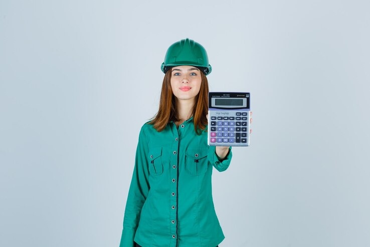 Kobieta w zielonym kasku i koszuli prezentuje kalkulator, prawdopodobnie do szacowania kosztów instalacji.