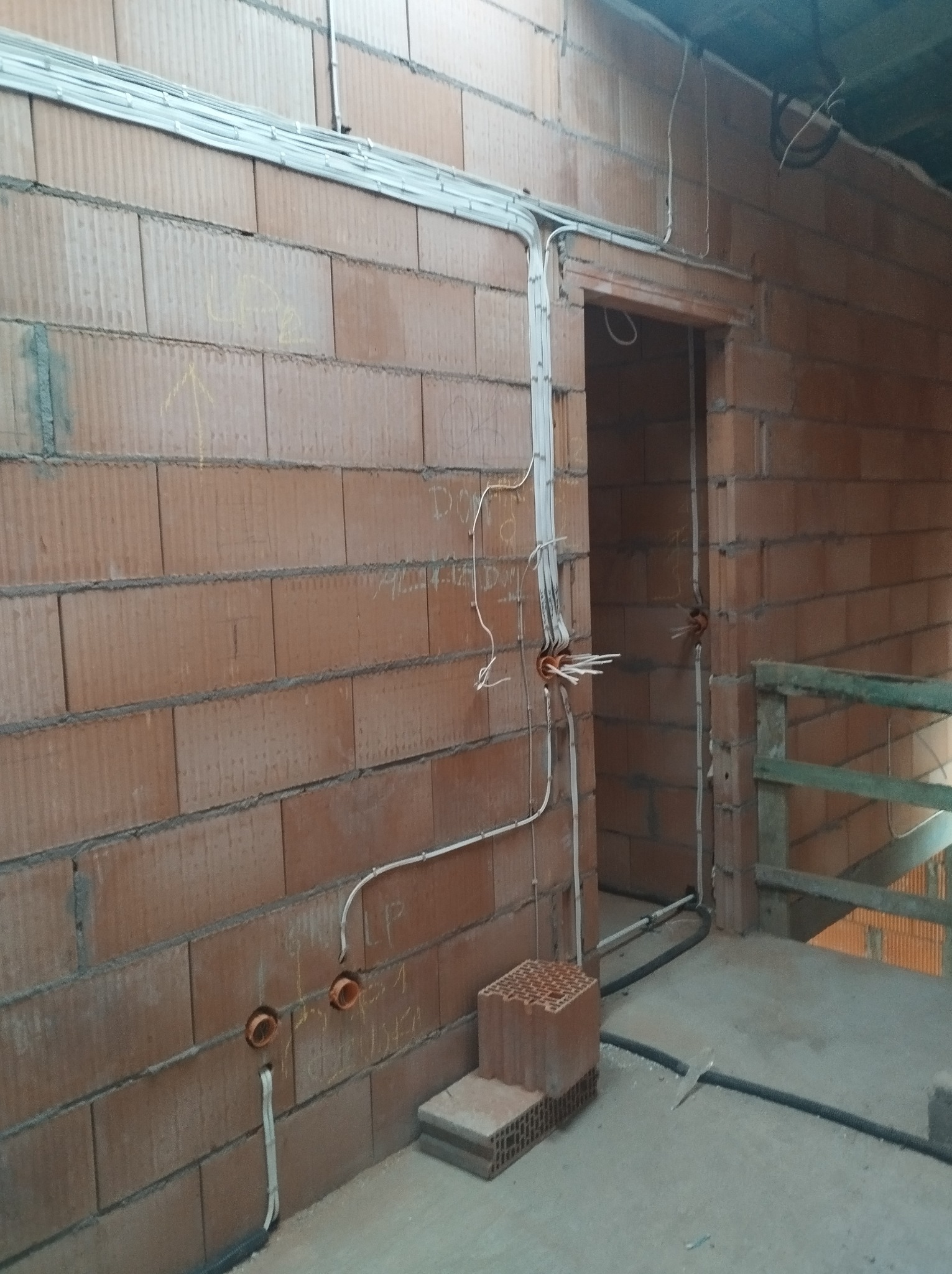 Surowy mur z instalacją elektryczną: kable w peszlach, puszki podtynkowe. Widoczne oznaczenia na ścianie. Etap prac instalacyjnych w nowym budynku.