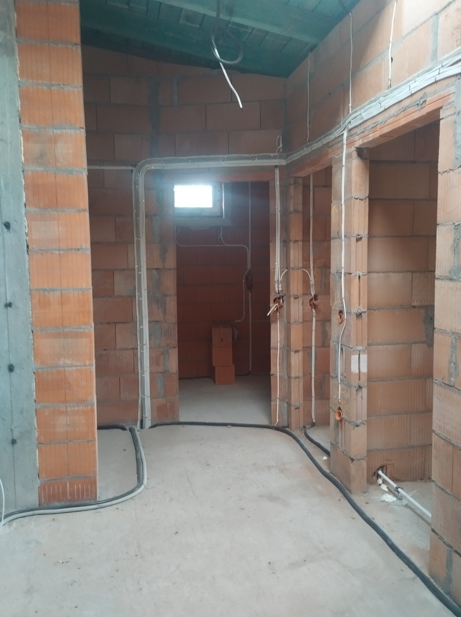 Instalacja elektryczna w surowym wnętrzu: kable w peszlach prowadzone po ścianach z cegły i pod sufitem. Widoczne puszki instalacyjne i przewody.