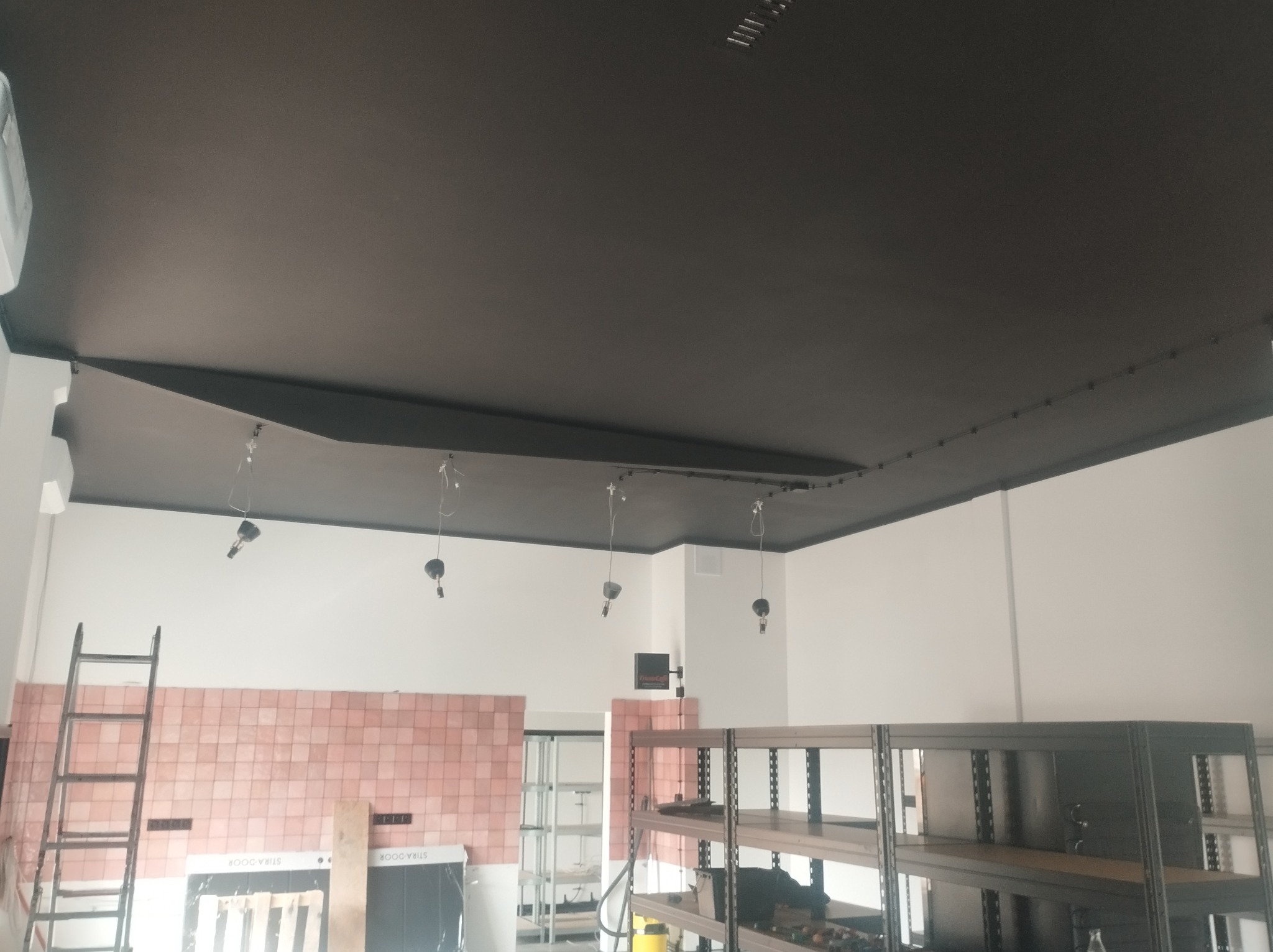 Czarne podwieszane sufity z punktowym oświetleniem w trakcie montażu. Widoczne kable i elementy instalacji. W tle drabina i regały.