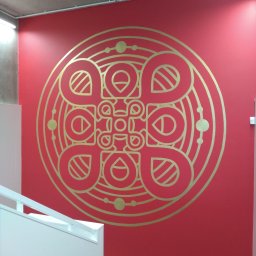 LEONID PODOLYAK MOREMURALS - Czerwona ściana w biurze z dużym, geometrycznym wzorem w kolorze złotym, widoczne fragmenty białej klatki schodowej.