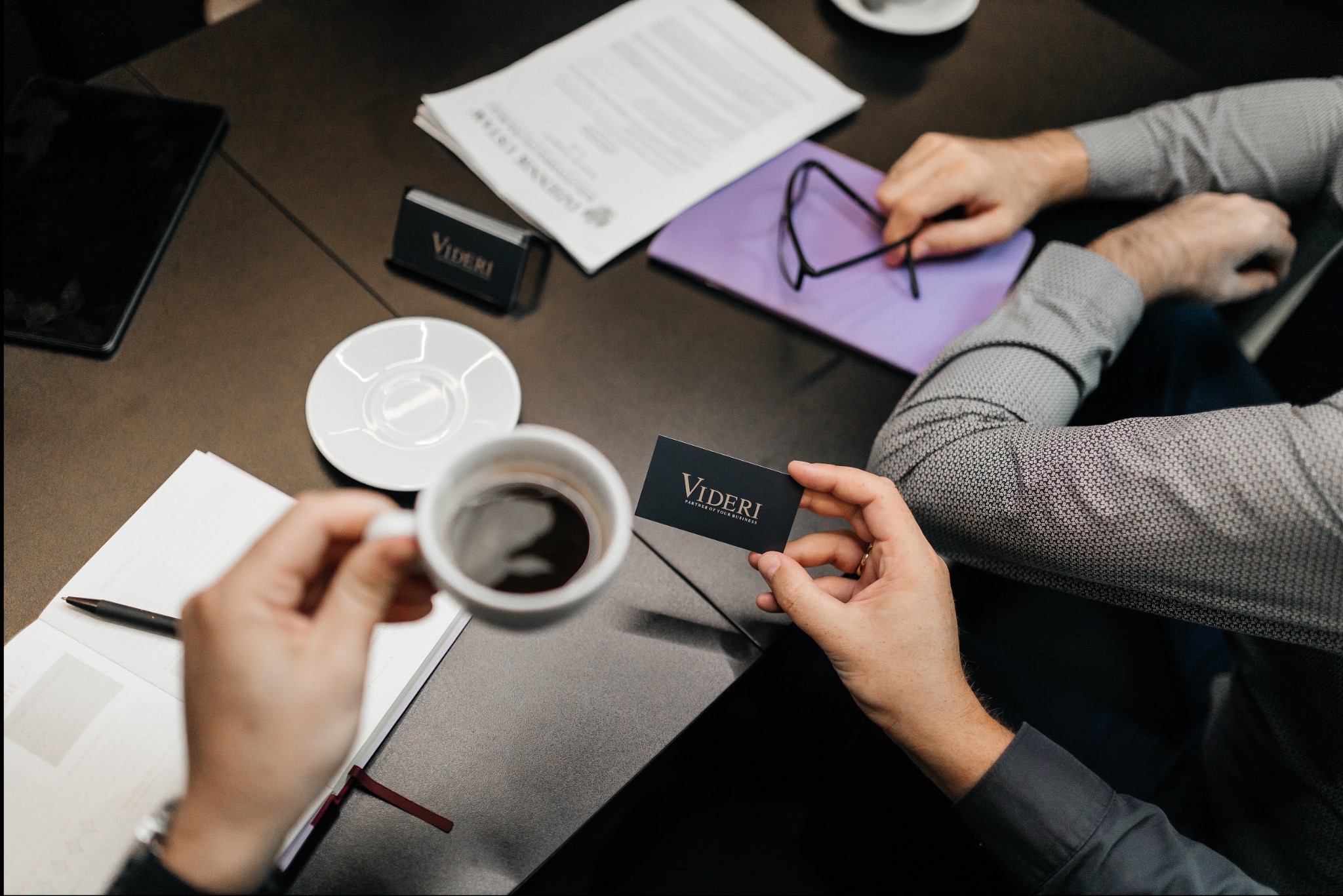 Spotkanie biznesowe przy kawie: wizytówka Videri, notatnik, tablet i dokumenty na stole. Elegancki, biznesowy klimat.