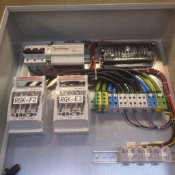 ENER-KRIS Krzysztof Bogucki - Wnętrze metalowej skrzynki rozdzielczej z zainstalowanymi bezpiecznikami RGK-F2 i RGK-E3, licznikiem energii elektrycznej LE-03M CT, listwami zaciskowymi z oznaczonymi fazami L1, L2, L3, N i PE...