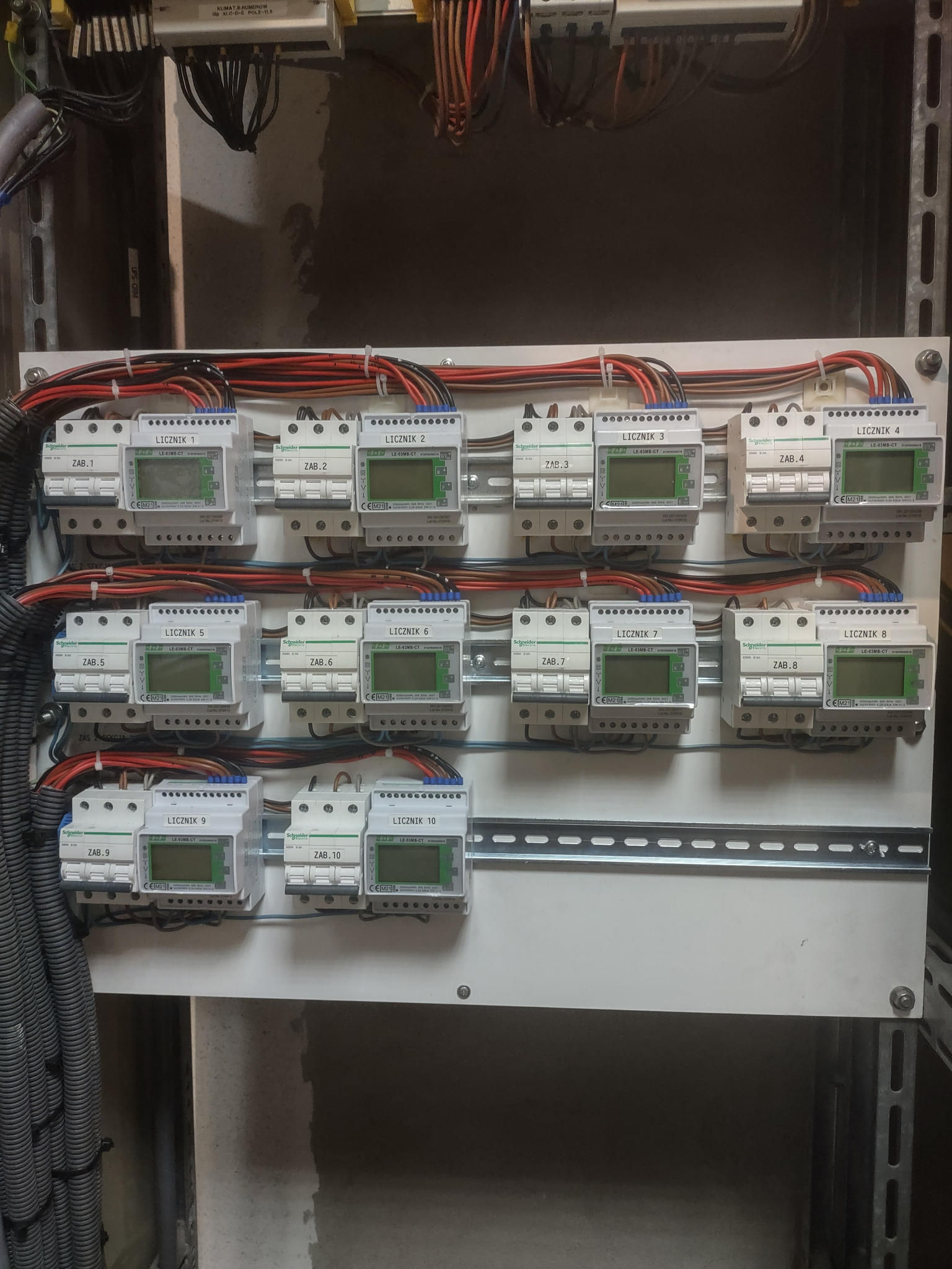 Rozdzielnica elektryczna z zamontowanymi licznikami energii elektrycznej Schneider Electric LE-03MB-CT, oznaczonymi numerami od 1 do 10, oraz bezpiecznikami oznaczonymi ZAB.1 do ZAB.10, połączone...