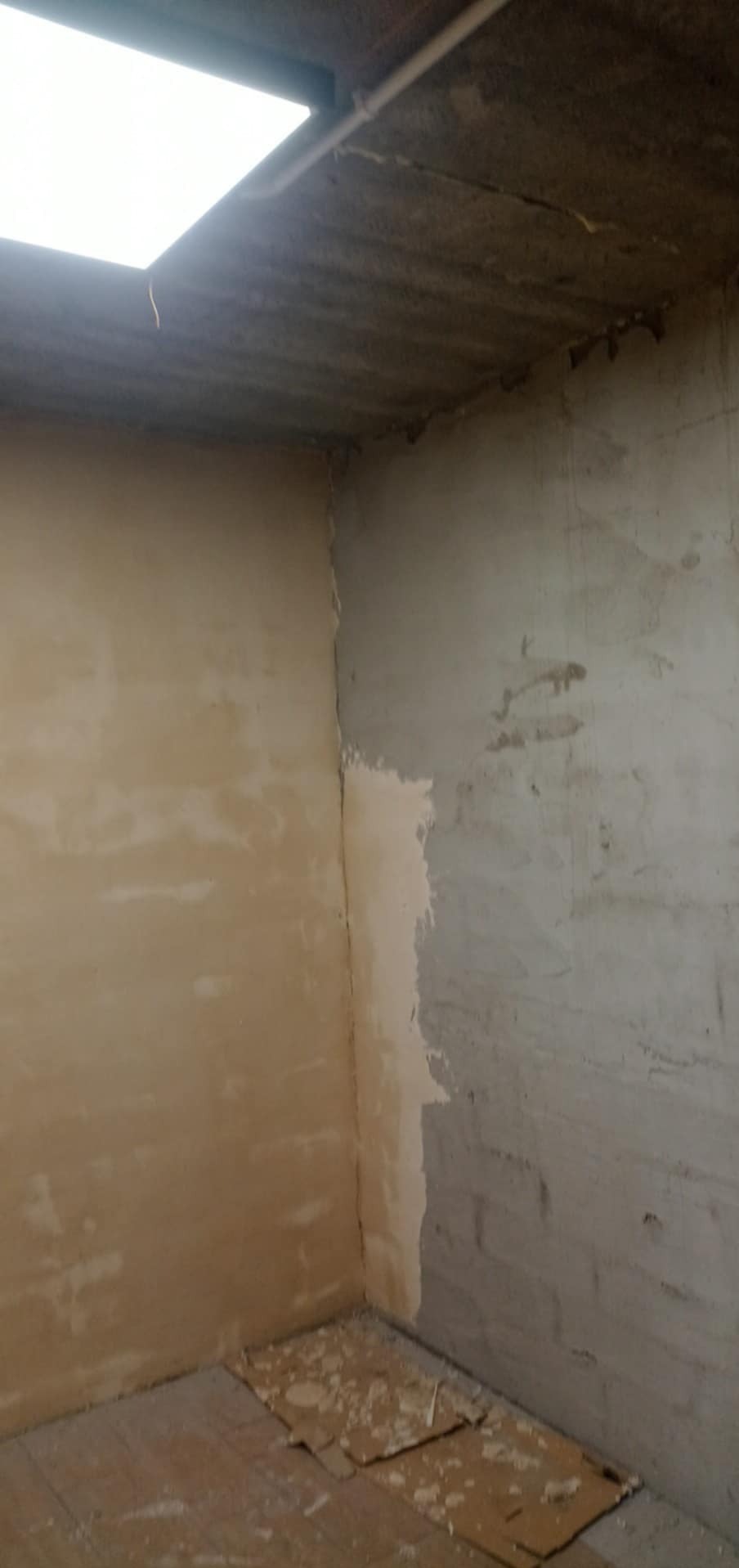 Fragment wnętrza w trakcie prac przygotowawczych do wykończenia ścian, widoczne ślady po szpachlowaniu i gruntowaniu, podłoga zabezpieczona kartonem.