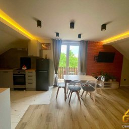 Goodhome - Jasne, przestronne poddasze po remoncie z aneksem kuchennym, stołem i krzesłami. Ceglana ściana z telewizorem, oświetlenie LED. Widok na zieleń za oknem.