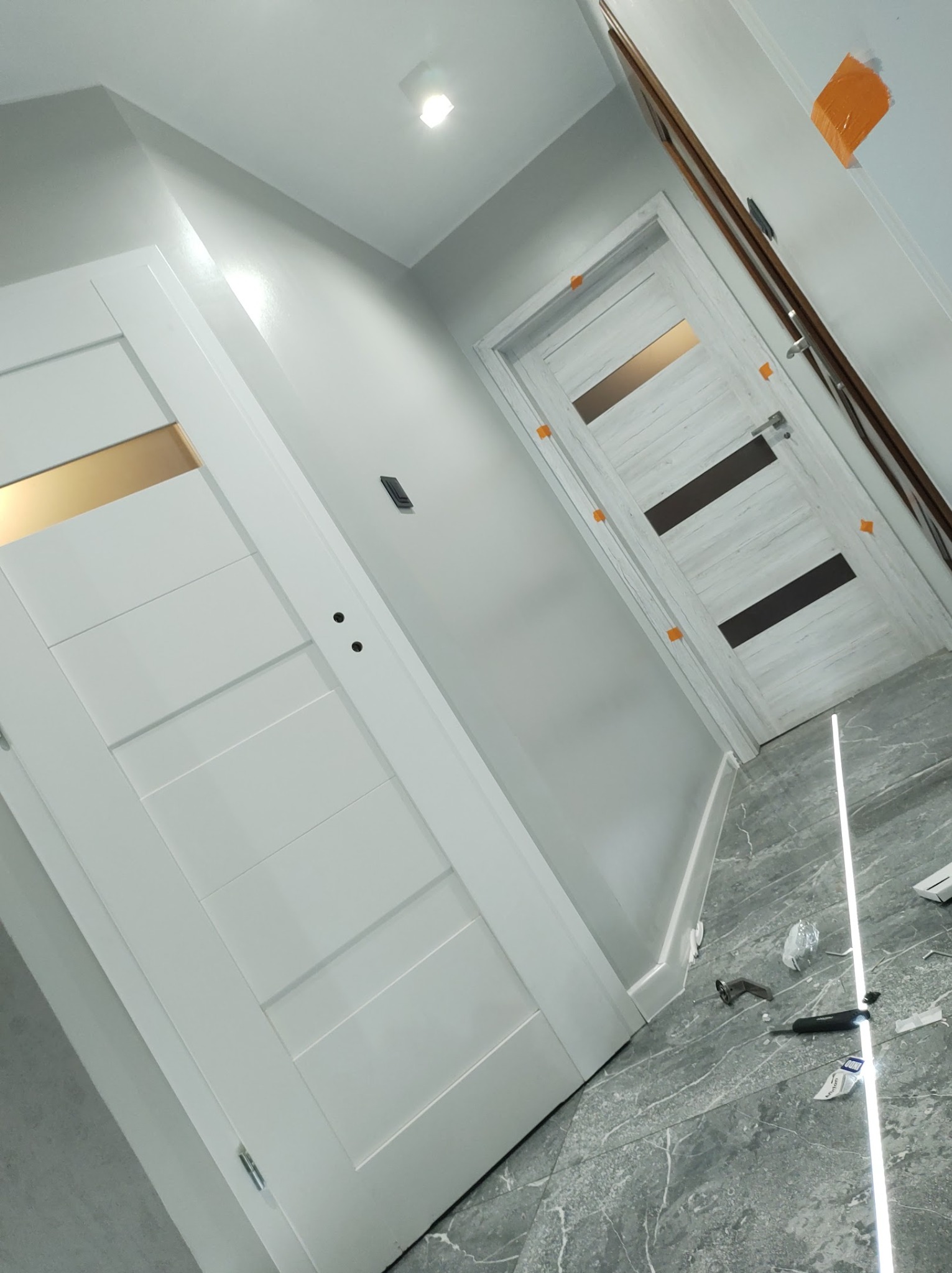 Montaż dwóch różnych modeli drzwi wewnętrznych w nowym mieszkaniu, widoczne narzędzia na podłodze z szarego marmuru.