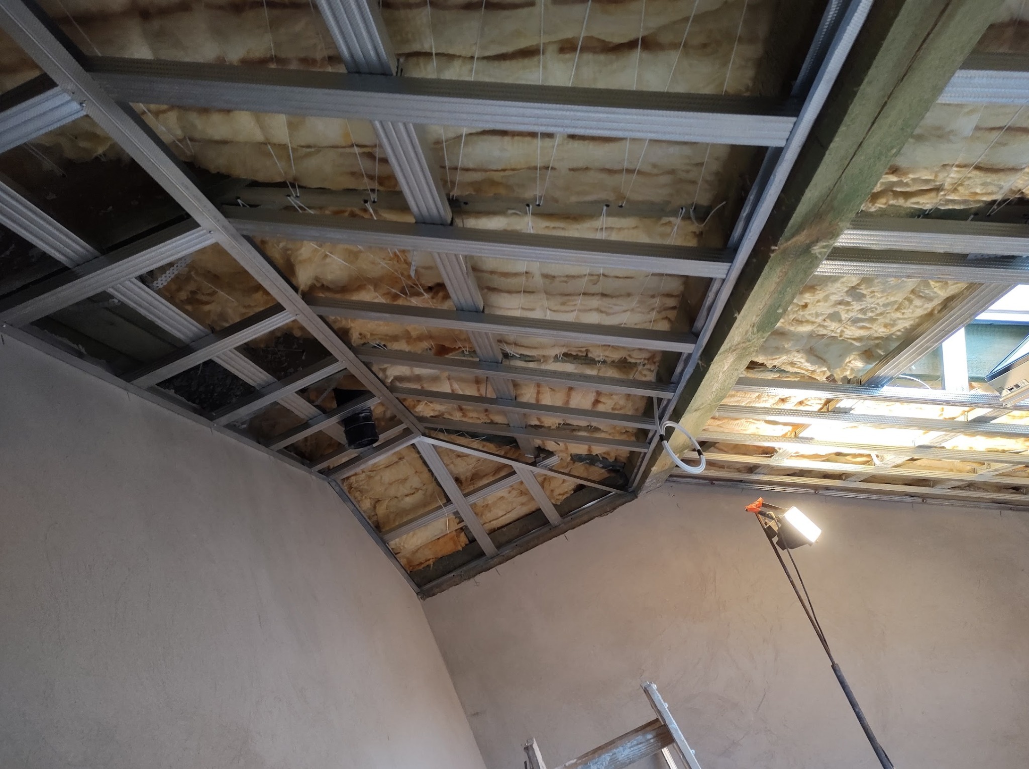 Montaż izolacji poddasza: widok na konstrukcję metalową, wełnę mineralną i lampę oświetlającą