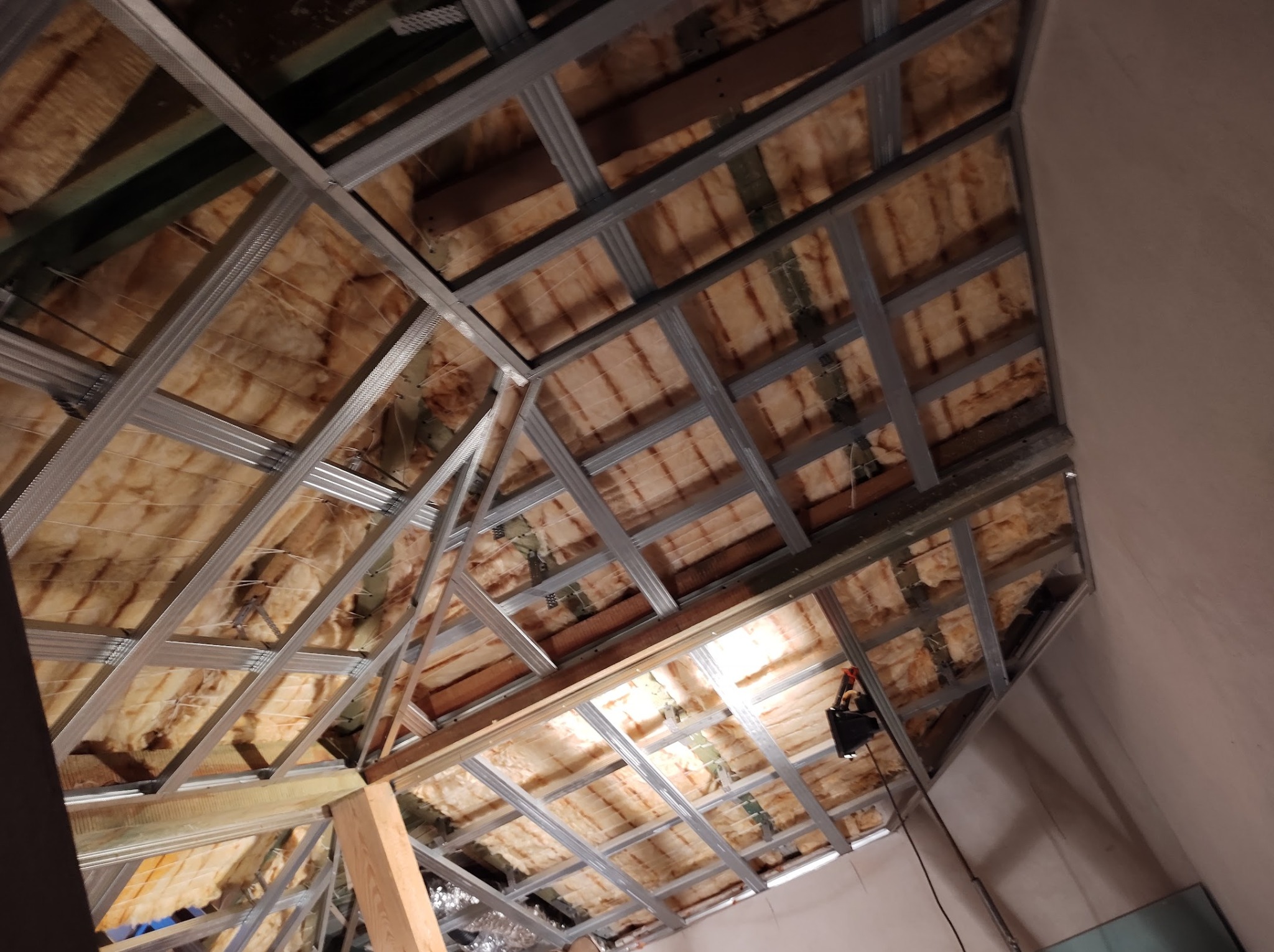 Montaż metalowego stelażu sufitu podwieszanego z izolacją z wełny mineralnej na poddaszu, widok z dołu pod kątem.