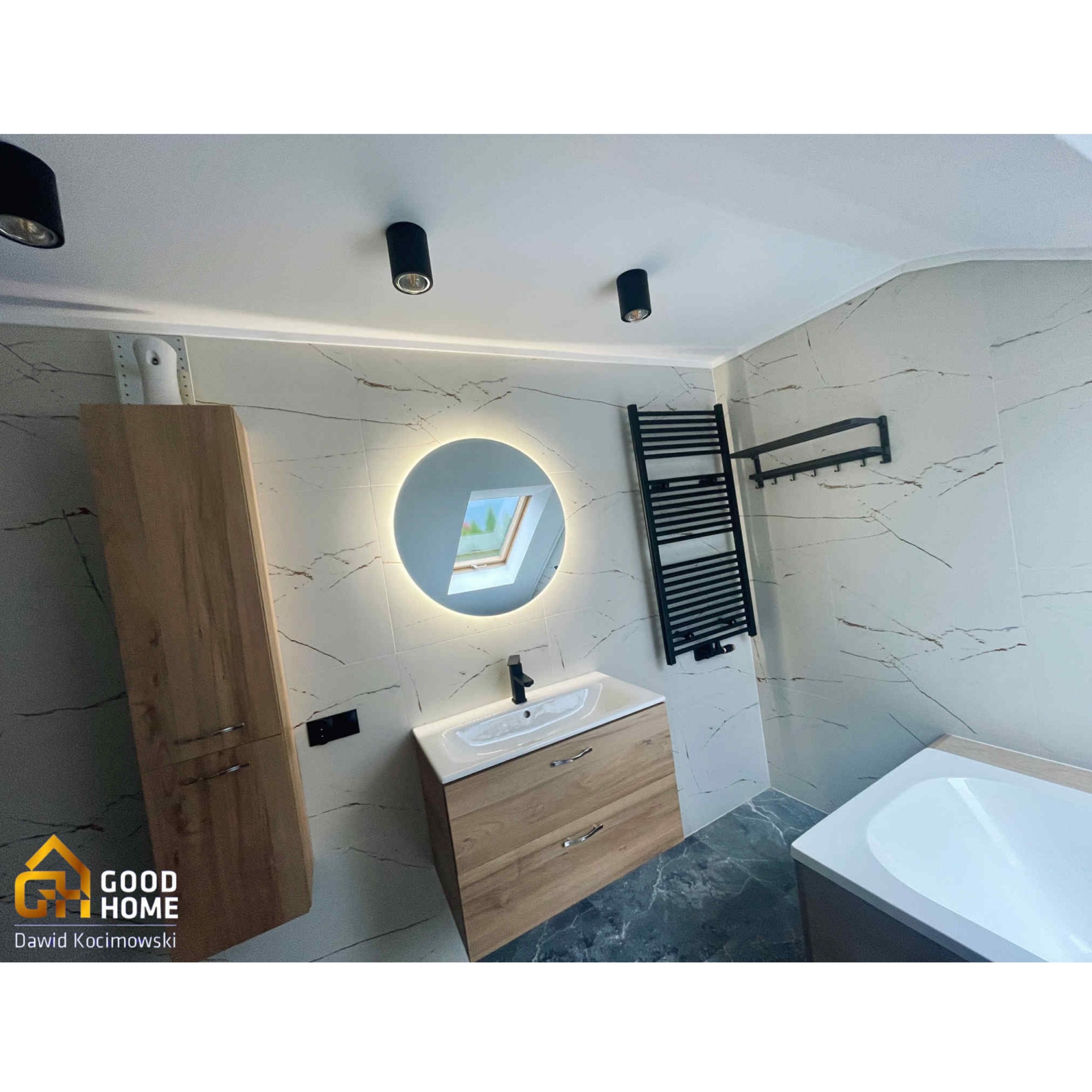 Nowoczesna łazienka z okrągłym lustrem LED, drewnianą szafką pod umywalką i marmurowymi płytkami. Czarny grzejnik drabinkowy dodaje elegancji.